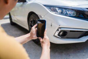 Accident victim taking pictures of their damages car, wondering, “Why is my car accident settlement taking so long?”