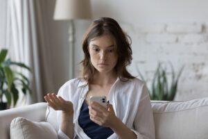 A shocked woman looking at her phone, wondering why her insurance went up for no reason.
